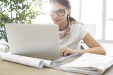 Junge Frau mit Brille arbeitet mit ihrem Laptop am Schreibtisch.