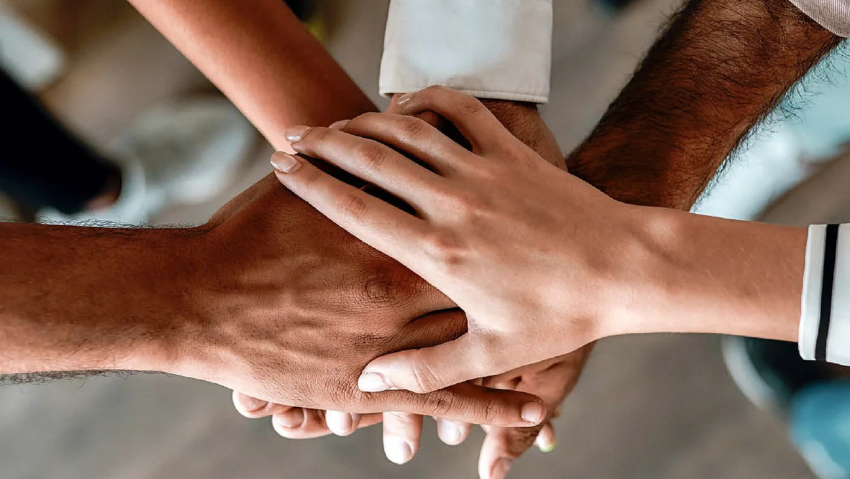 Die Hände verschiedener Personen sind überinander gestapelt, um Zusammenhalt zu zeigen