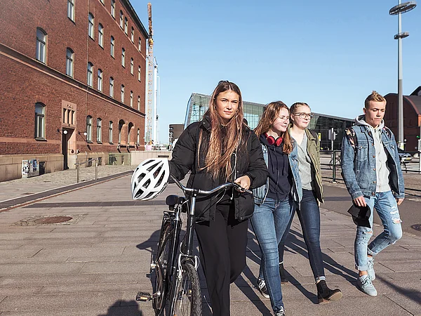Gruppe Teenager läuft durch Fußgängerbereich. Ein Mädchen links schiebt ein Fahrrad.