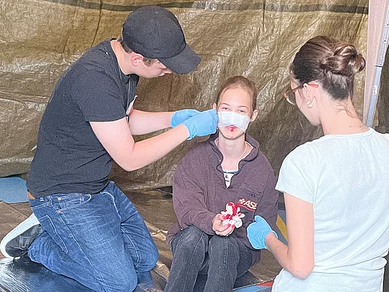 Eine Schulsanitäterin und ein Schulsanitäter verbinden eine verletzte Mitschülerin