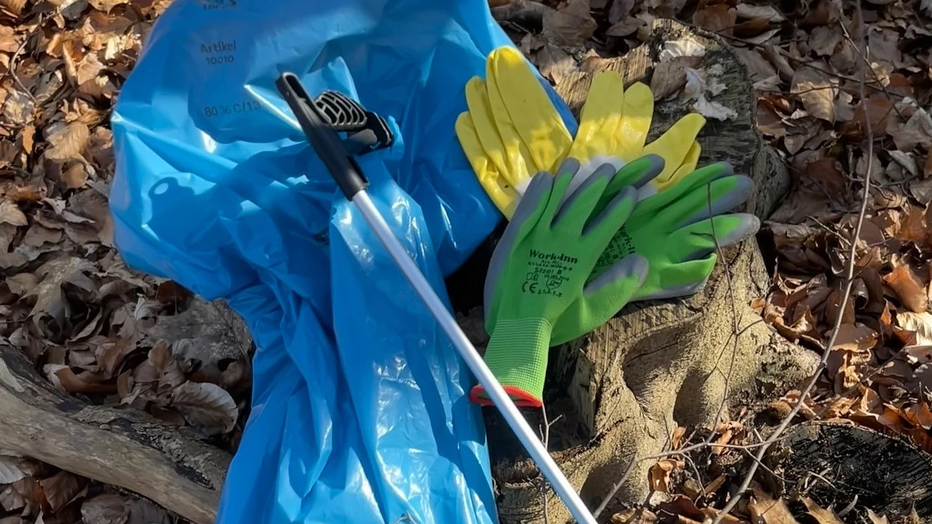 Eine Müllzange, ein Paar Arbeitshandschuhe und eine Müllzange liegen auf eine laubbedeckten Waldboden